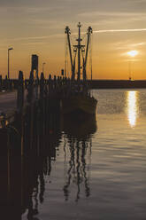 Denmark, Romo, Fishing boat moored to wooden pier at sunset - ASCF01147