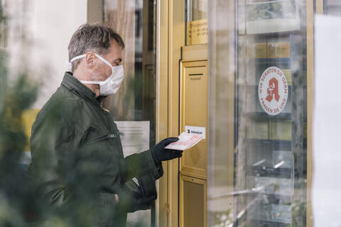 Mann mit Maske wartet vor einer Apotheke und hält ein Rezept in der Hand, lizenzfreies Stockfoto