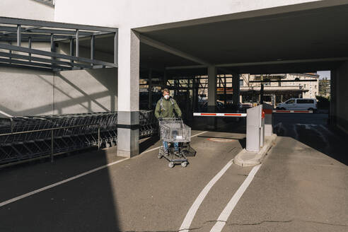 Man with mask pushing shopping cart outside supermarket - MFF05133