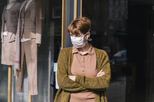Woman wearing mask standing in front of her closed clothing store - MFF05140