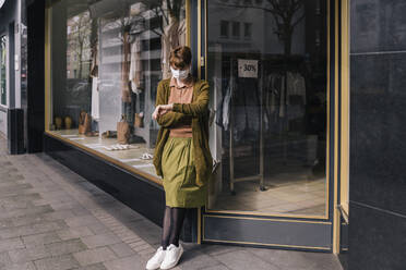 Frau mit Maske steht vor ihrem geschlossenen Bekleidungsgeschäft - MFF05142