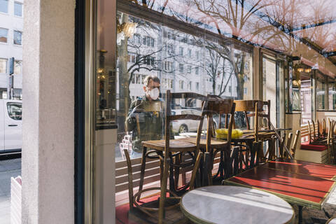 Mann mit Maske schaut durch ein Fenster in ein geschlossenes Restaurant, lizenzfreies Stockfoto