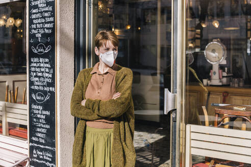 Woman wearing mask standing in front of her closed restaurant - MFF05146