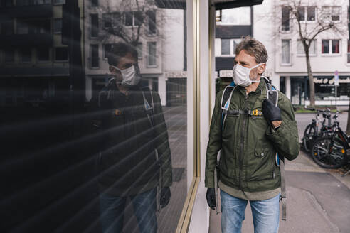 Man with mask looking through window into closed store - MFF05149