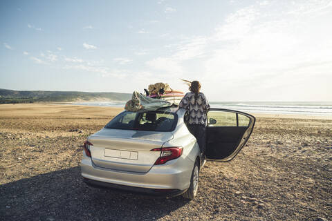 Rückenansicht einer Frau mit Auto am Strand mit Blick aufs Meer, Tafedna, Marokko, lizenzfreies Stockfoto