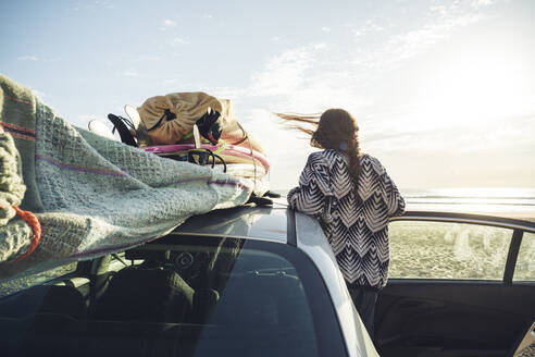 Rückenansicht einer Frau mit Auto am Strand mit Blick aufs Meer, Tafedna, Marokko - HBIF00083