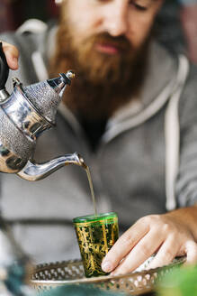 Mann gießt Tee in ein grünes Glas - DGOF00551