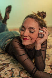 Porträt einer jungen Frau, die auf dem Boden liegt und mit Kopfhörern Musik hört - MPPF00676