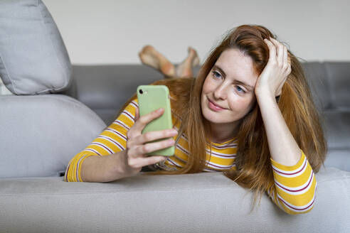 Young woman lying on the couch at home using smartphone - AFVF05775