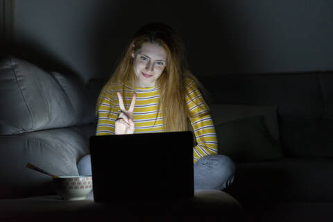 Junge Frau mit einer Laptop-Videokonferenz auf der Couch zu Hause, lizenzfreies Stockfoto