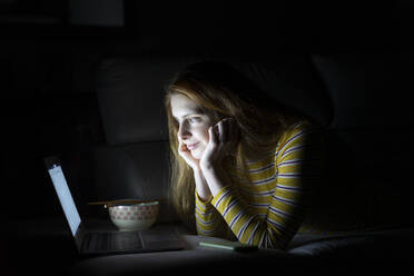 Junge Frau liegt auf der Couch zu Hause und benutzt einen Laptop - AFVF05782