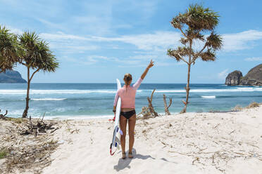 Rückansicht einer Surferin mit Surfbrett am Strand, Sumbawa, Indonesien - KNTF04497