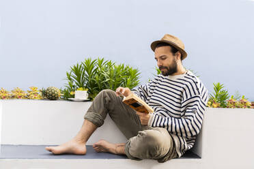 Man sitting on balcony reading a book - AFVF05797