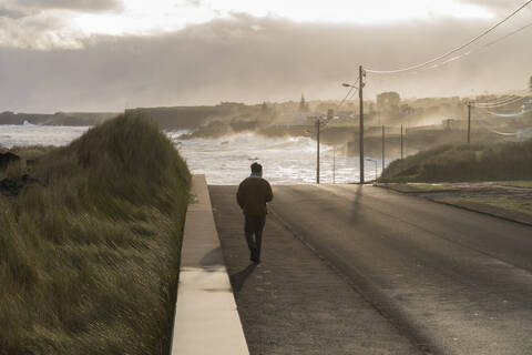 Rear view of man walking on a road at the coast, Sao Miguel Island, Azores, Portugal stock photo