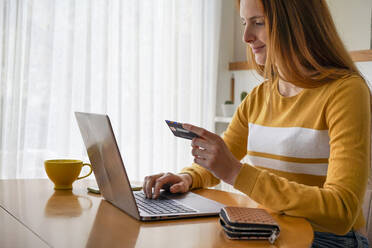 Young woman with credit card using laptop at home - AFVF05825