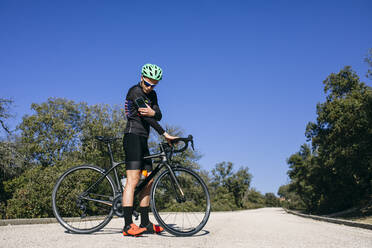 Diabetic cyclist checking his sugar level during a break on country road - ABZF03068