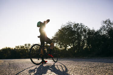 Radfahrer, der während einer Pause auf einer Landstraße bei Sonnenuntergang aus einer Flasche trinkt - ABZF03072