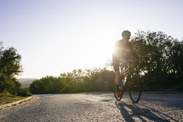 Sportler fährt Fahrrad auf Landstraße bei Sonnenuntergang - ABZF03073