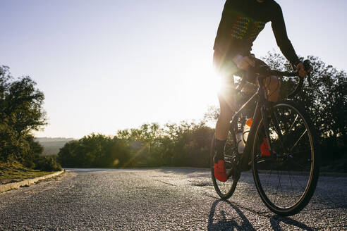 Nahaufnahme eines Sportlers beim Fahrradfahren auf einer Landstraße bei Sonnenuntergang - ABZF03074
