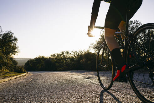 Nahaufnahme eines Sportlers beim Fahrradfahren auf einer Landstraße bei Sonnenuntergang - ABZF03075
