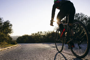 Close-up of athlete riding bicycle on country road at sunset - ABZF03076