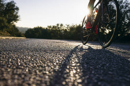 Nahaufnahme eines Sportlers beim Fahrradfahren auf einer Landstraße bei Sonnenuntergang - ABZF03077