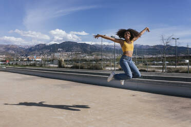 Porträt einer glücklichen jungen Frau, die in die Luft springt, Spanien - TCEF00313