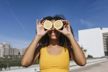 Portrait of laughing young woman covering eyes with lemon halves - TCEF00314