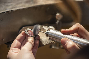 Hand einer Goldschmiedin bei der Arbeit mit einem Schleifgerät an einem Silberring - VPIF02156