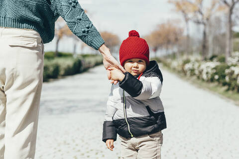 Porträt eines kleinen Jungen, der die Hand seiner Mutter hält und eine rote Pudelmütze trägt, lizenzfreies Stockfoto