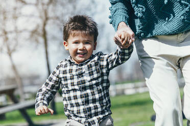 Porträt eines glücklichen kleinen Jungen, der Hand in Hand mit seiner Mutter in einem Park läuft - JCMF00441