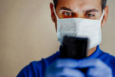 Arzt mit Gesichtsmaske, der ein Smartphone benutzt - CJMF00271