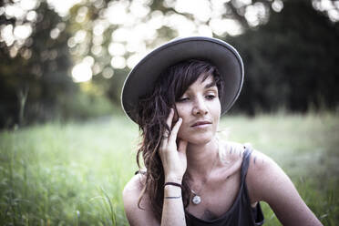 Natural girl with freckles and tattoos sits peacefully in long grass - CAVF77609