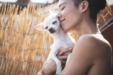 Schöne Frau und kleiner Hund lächeln und umarmen sich in der Nachmittagssonne - CAVF77618