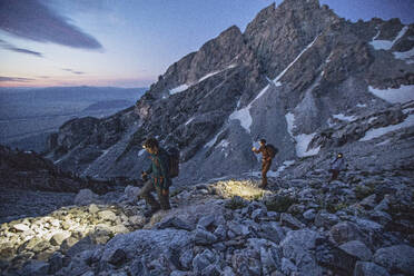 Three hikers with lights walk along a trail in the Tetons, sunrise - CAVF77623