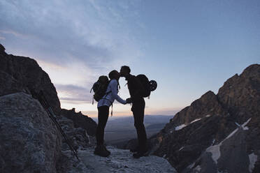 Zwei Wanderer mit Rucksäcken küssen sich bei Sonnenaufgang in den Bergen, Wyoming - CAVF77624