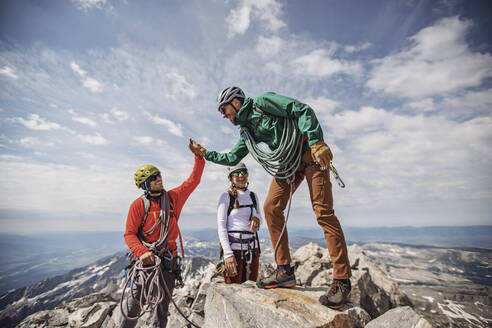 Zwei Männer beim High-Five auf dem Gipfel des Grand Teton, während eine dritte Person zusieht - CAVF77628