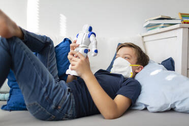 Boy with mask playing in his room during the corona crisis with his new, only friend, a robot - HMEF00827