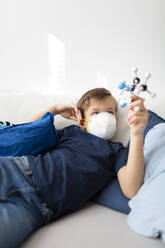 Junge mit Maske spielt in seinem Zimmer mit einem Molekularmodell während der Koronakrise zu Hause - HMEF00830