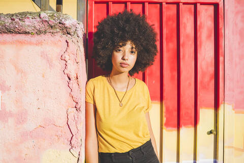 Porträt einer jungen Frau mit Afrofrisur, die an einer Wand lehnt, lizenzfreies Stockfoto