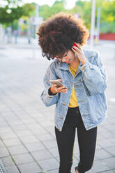 Young woman with afro hairdo using smartphone and headphones in the city - MEUF00241