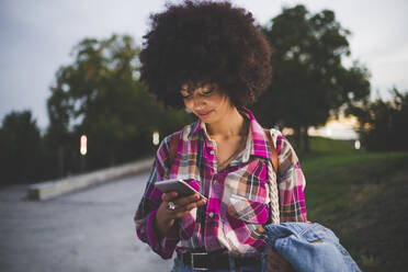 Young woman with afro hairdo using smartphone outdoors at dusk - MEUF00260