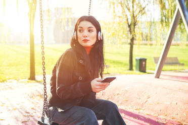 Beautiful woman sitting on a swing and listening to music - MEUF00291