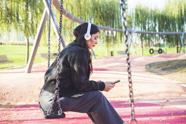Beautiful woman sitting on a swing and listening to music - MEUF00292