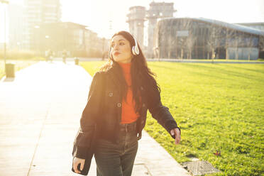 Beautiful woman walking in a park and listening to music - MEUF00295