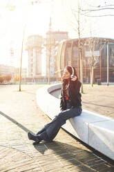 Schöne Frau, die auf einer Bank sitzt und ihr Smartphone benutzt, um Musik zu hören - MEUF00296