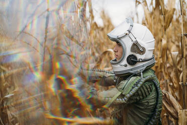 Young spaceman standing in wilted corn field - JCMF00450