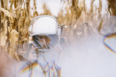 Young spaceman standing in wilted corn field - JCMF00456