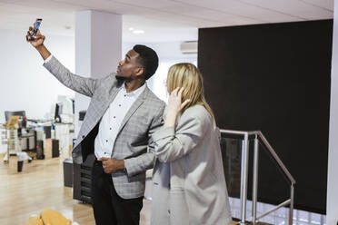 Young businessman and businesswoman taking a selfie in office - LJF01475