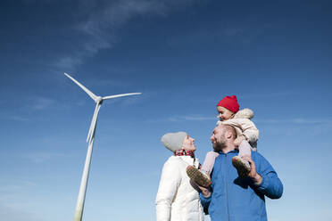 Glückliche Eltern mit kleiner Tochter gegen den Himmel mit Windrad im Hintergrund - VYF00065